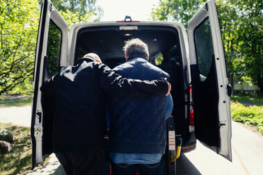 Kuljettaja auttaa asiakasta nousemaan Matkapalvelun auton kyytiin.