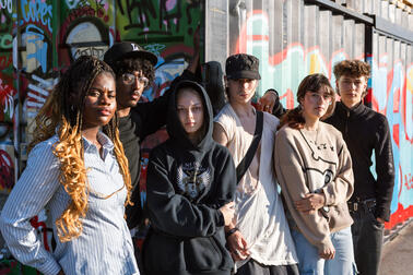 Group of young people standing in front of a graffiti wall.