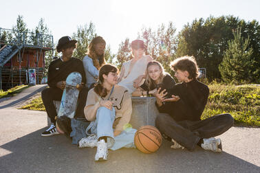 A group of cheerful young people sitting on an asphalt court with a basketball.