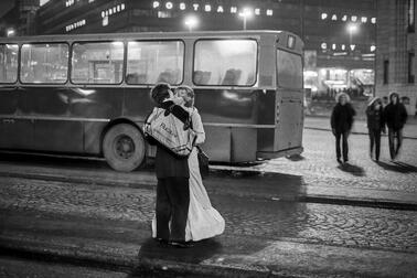 Mustavalkoinen kuva, jossa mies ja nainen suutelevat, bussi taustalla.