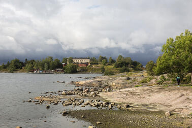 Harakan saari Kaivopuistosta katsottuna. Etualalla kalliota ja taustalla rakennuksia.