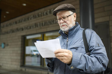 Ulkovaatteisiin pukeutunut mies katsoo kädessään olevaa paperia.