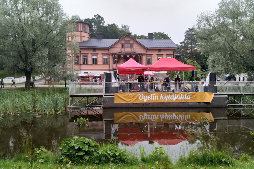 Kuvassa Oulunkylän Seurahuone ja edustalla telttoja ja ihmisiä sekä Ogelin kyläjuhla -lippu.