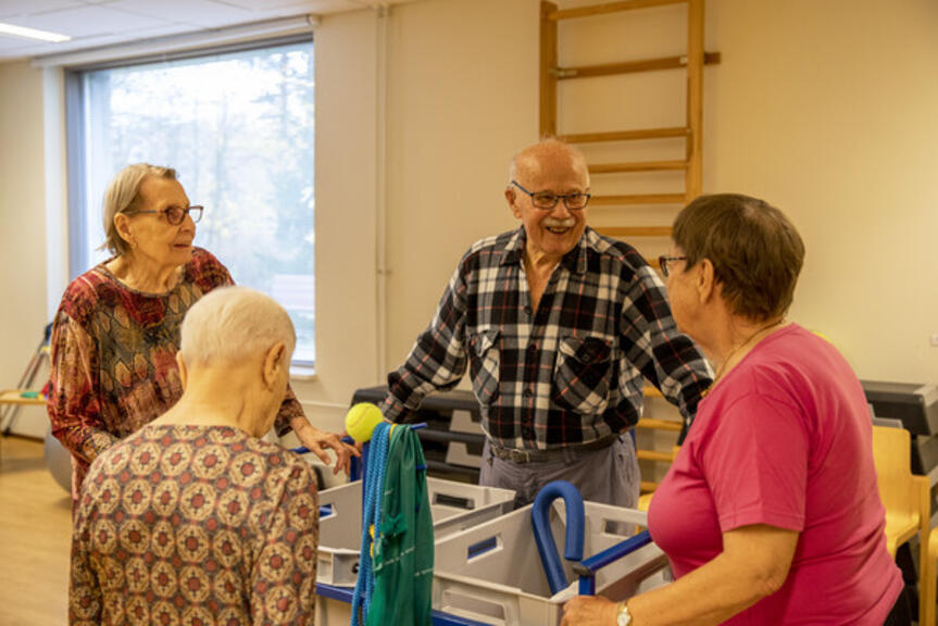 Neljä henkilöä seisoo liikuntasalissa ringissä. Neljä henkilöä seisoo liikuntasalissa ringissä.