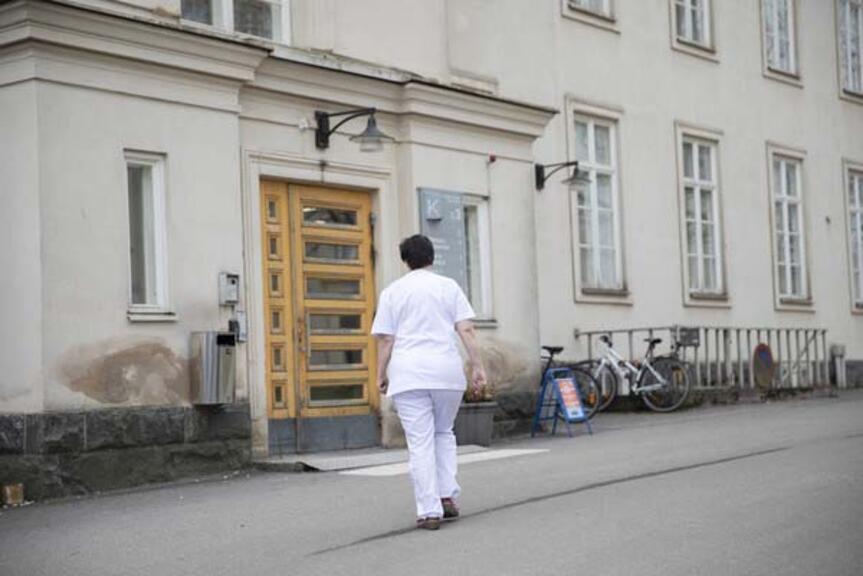 Hoitaja kävelee kohti sairaalan ulko-ovea. Hoitaja kävelee kohti sairaalan ulko-ovea.