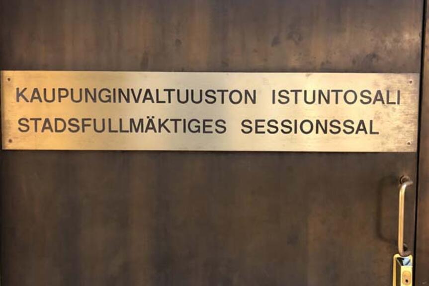 Kaupunginvaltuuston istuntosalin kupariovi nimikyltteineen.