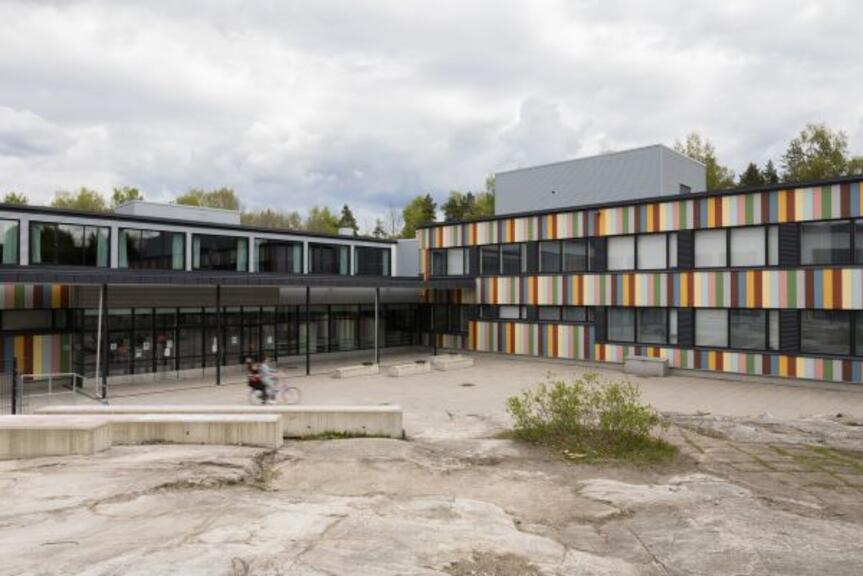 Nuori kyyditsee polkupyörällä toista nuorta koulun pihalla pilvisenä kesäpäivänä. Nuori kyyditsee polkupyörällä toista nuorta koulun pihalla pilvisenä kesäpäivänä.