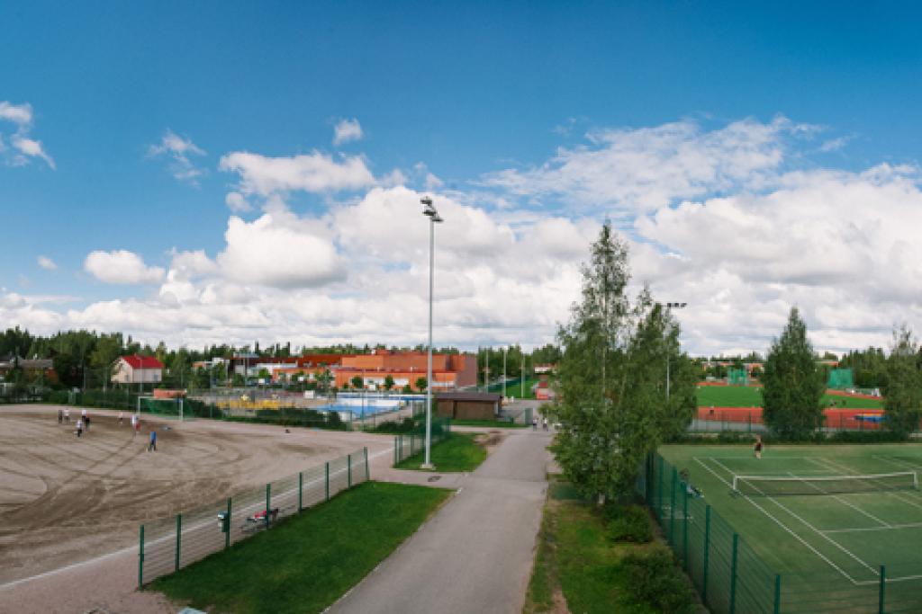 Yläilmoista otettu kuva liikuntapuistosta, jossa etualalla hiekka- ja tenniskenttiä, taaempana yleisurheilukenttä.