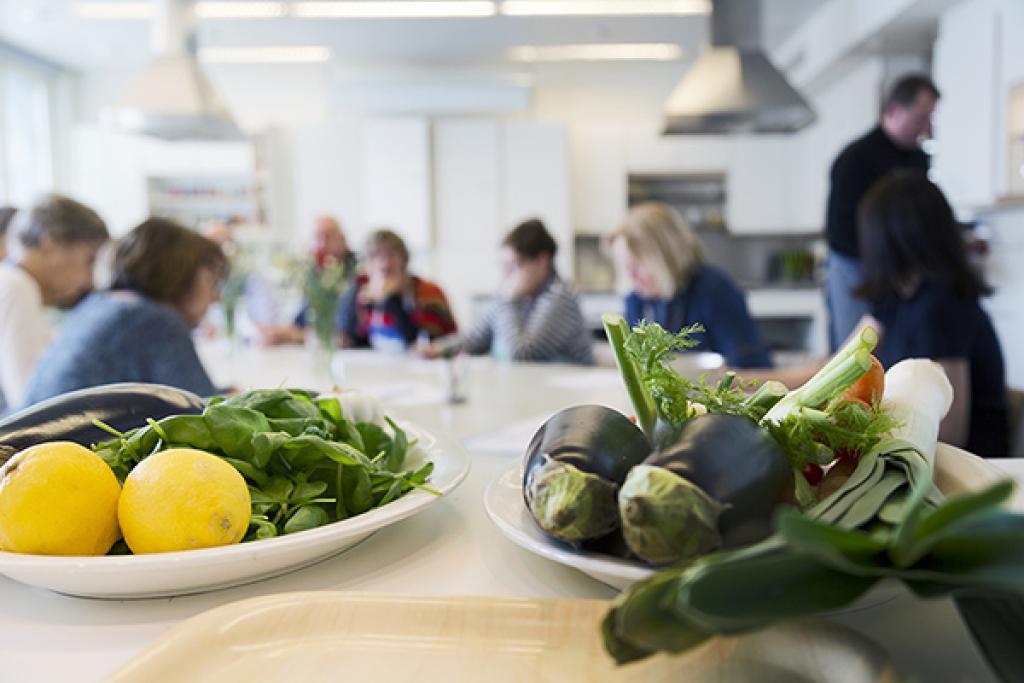 Etualalla vihanneksia ja sitruunoita lautasilla, taustalla opiskelijoita kotitalousluokassa.