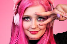 Vaaleanpunatukkainen nuori nainen kuulokkeet korvilla.