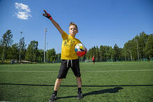 Lapsi tuulettaa jalkapallokentällä pallo kainalossaan.