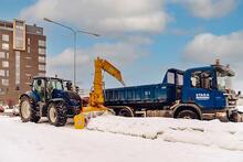 Tiivistävä lumilinko kiinnitettynä traktoriin syöttää lunta Staran kuorma-auton lavalle kaupungissa. 