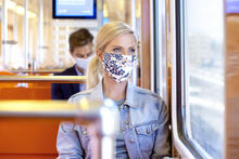 Nainen istuu metrossa maski päässä.