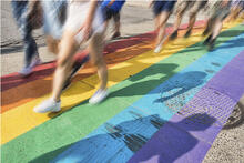 Ihmisiä kävelemässä sateenkaaren värein maalatulla kadulla.